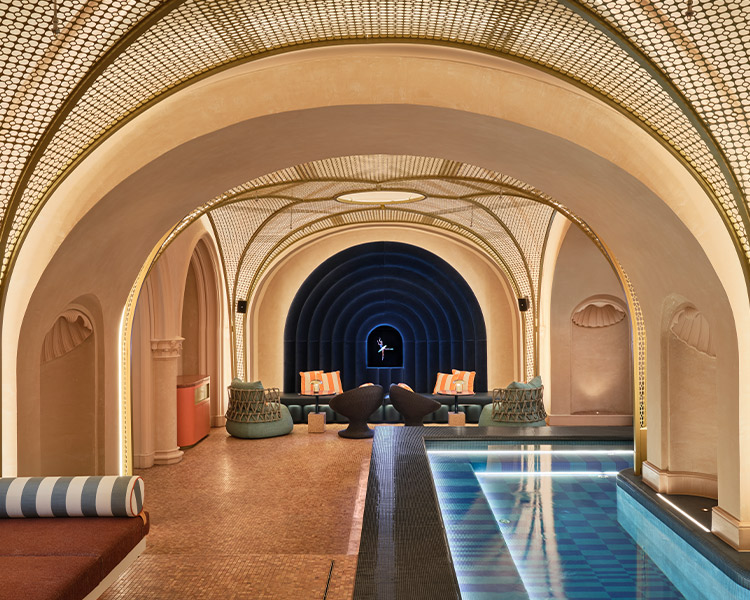 Luxurious indoor pool room with an arched mosaic ceiling, elegant arched doorways, a central narrow pool, and stylish lounge seating areas. the decor features warm golden and azure blue tones.