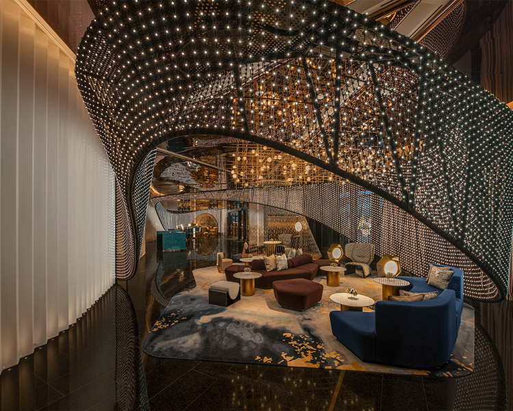 A luxurious hotel lobby featuring a sweeping curved structure adorned with sparkling lights. elegant seating areas with plush velvet sofas and round tables are set under a dramatic, illuminated archway.