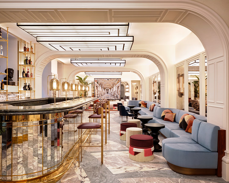 Elegant bar interior with a long, sleek counter, colorful plush seating, and arched doorways leading to a bright, inviting space beyond. the design features classic and modern elements.