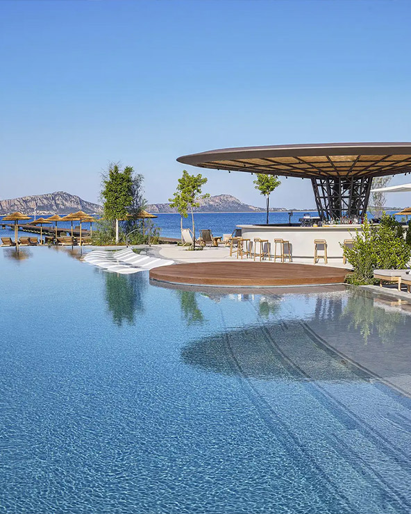 An elegant resort infinity pool overlooking a serene lake, with stylish seating under a modern canopy and a scenic mountain backdrop.