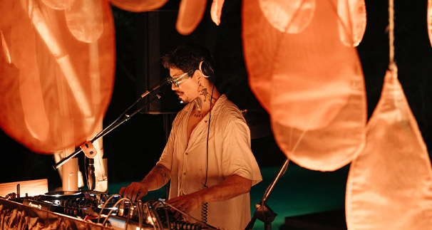 A dj mixing music at a night event, surrounded by illuminated, oversized pink decorations hanging above the dj booth, creating a vibrant and immersive atmosphere.