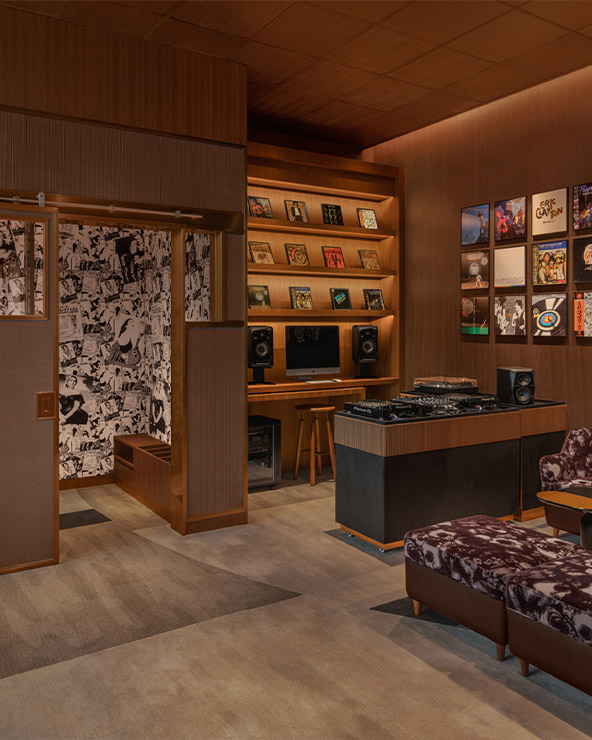 A cozy, well-appointed room featuring a large collection of vinyl records on wooden shelves, a vintage stereo system, rich wooden paneling, patterned armchairs, and modern artwork on the walls.