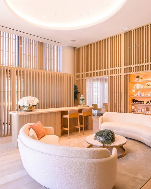 Modern, elegant lobby with curved, plush sofas, a wooden reception desk, vertical wooden slats on walls, and a cozy seating area. soft lighting and a warm color scheme create a welcoming atmosphere.