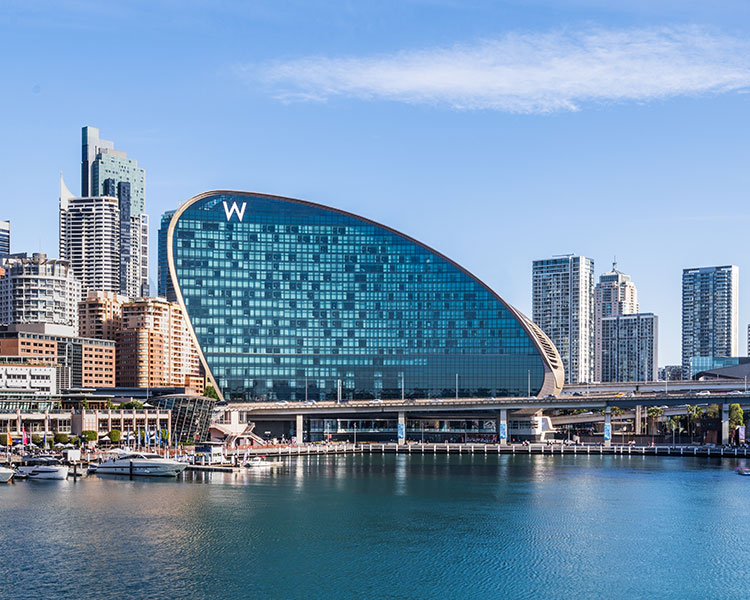 A waterfront view of a modern cityscape includes a prominent, uniquely shaped building with a large 