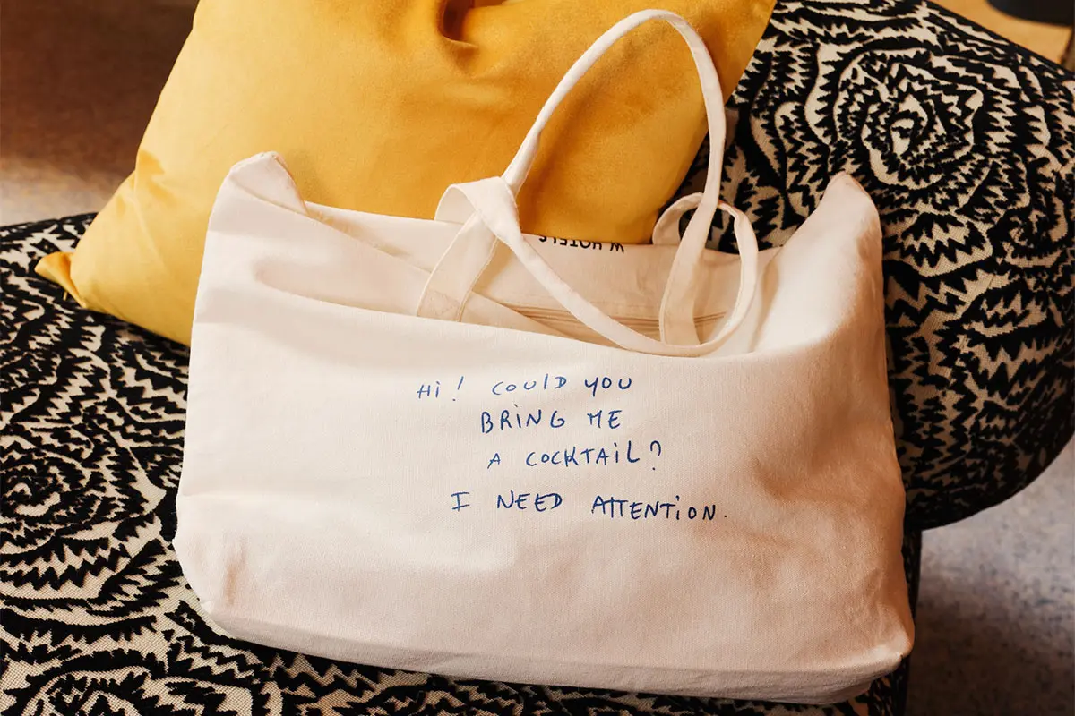 A white tote bag with blue handwritten text that reads, 