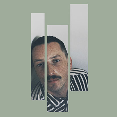 A man with short hair and a mustache, wearing a black and white striped shirt, is seen through three vertical rectangular cutouts on a muted green background.