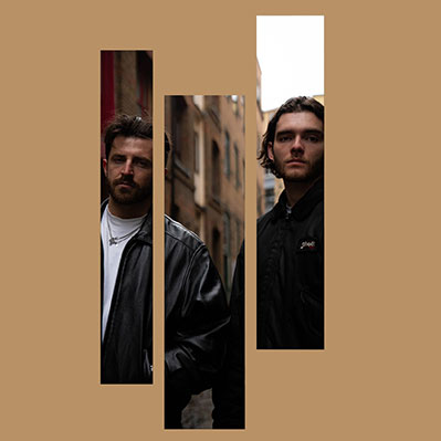 Two men stand in an alleyway, their images visible through three vertical rectangular cutouts on a solid brown background. Both have dark hair and wear dark jackets, looking directly at the camera.