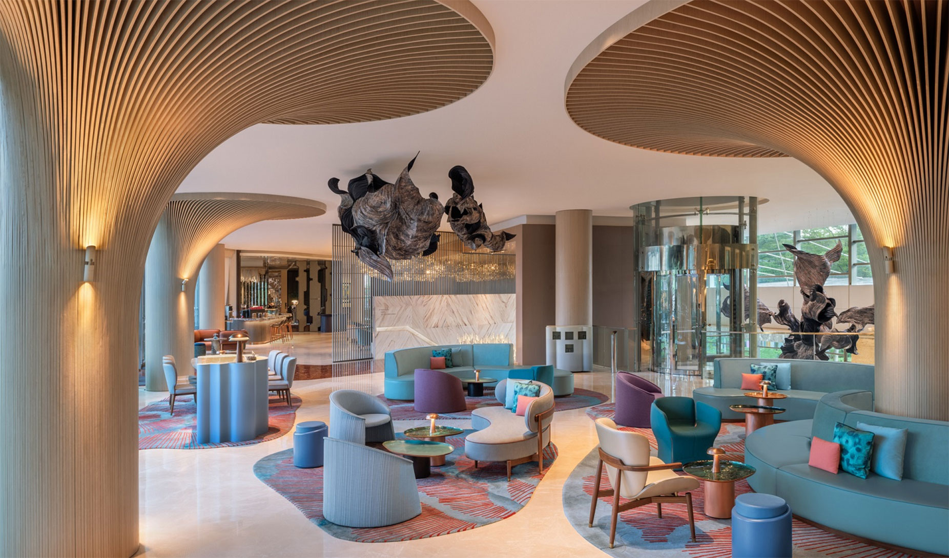 A modern hotel lobby with curved columns, sculptural ceiling art, round tables, colorful chairs, and soft lighting, creating a stylish and inviting atmosphere.