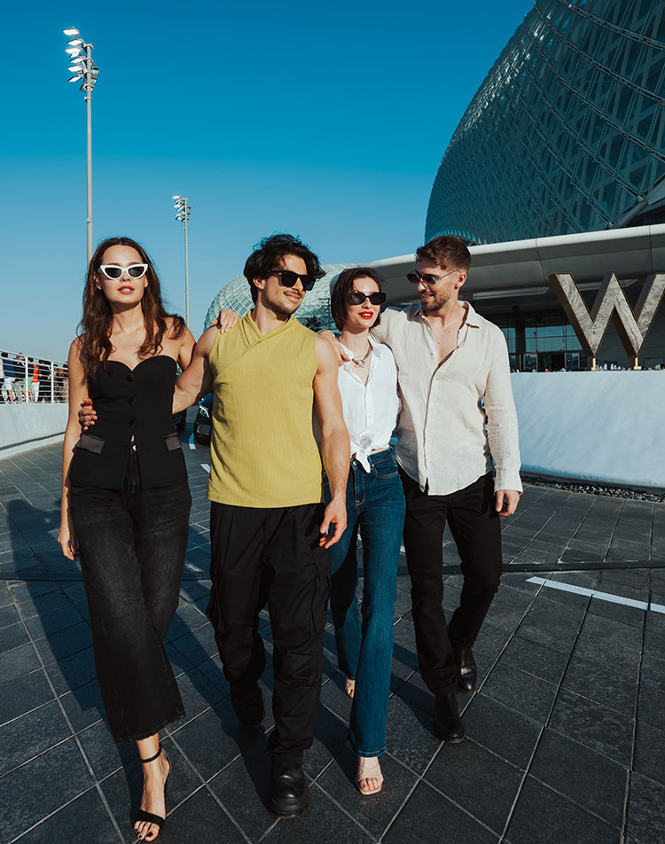 Four stylish young adults walk together outdoors near a modern building with a large 