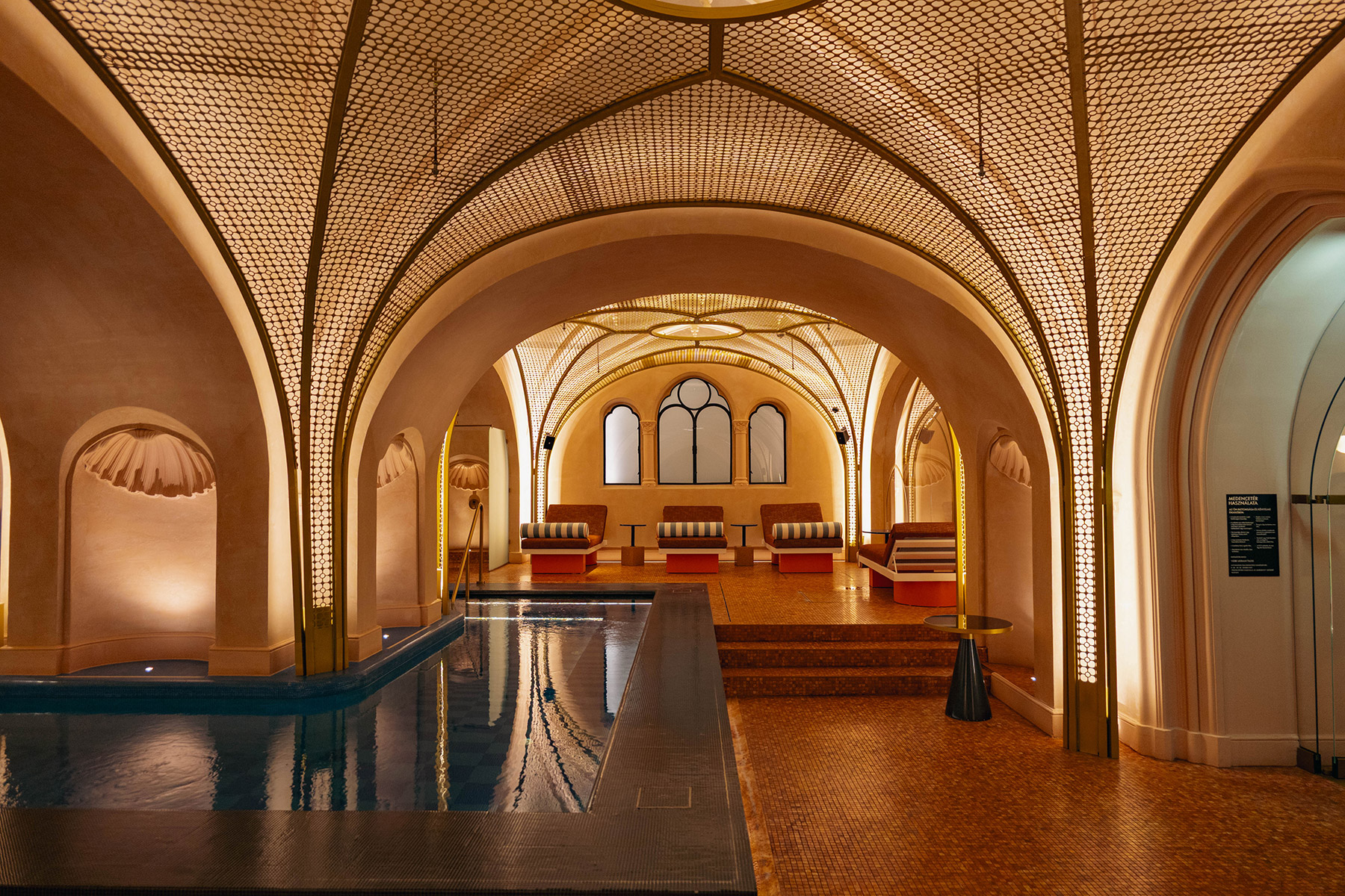 Luxurious indoor pool with arched ceilings and warm lighting, featuring ornate architectural details, lounge seating, and a serene, inviting atmosphere.