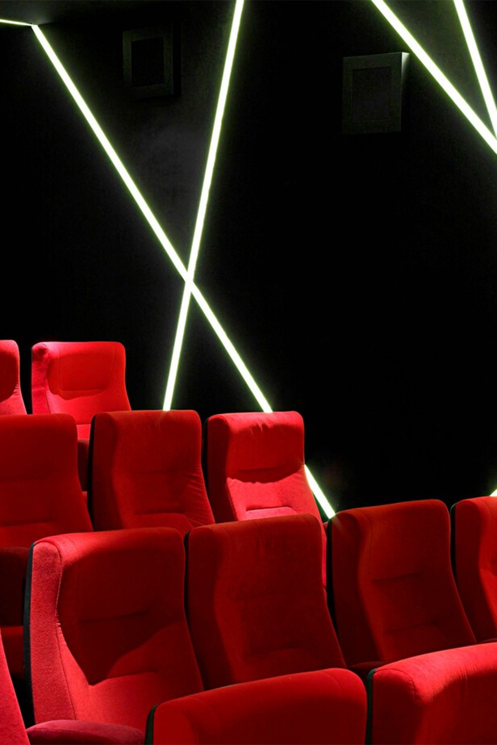 Rows of empty red theater seats face a black wall with diagonal, glowing white light strips, creating a modern and stylish cinema atmosphere.